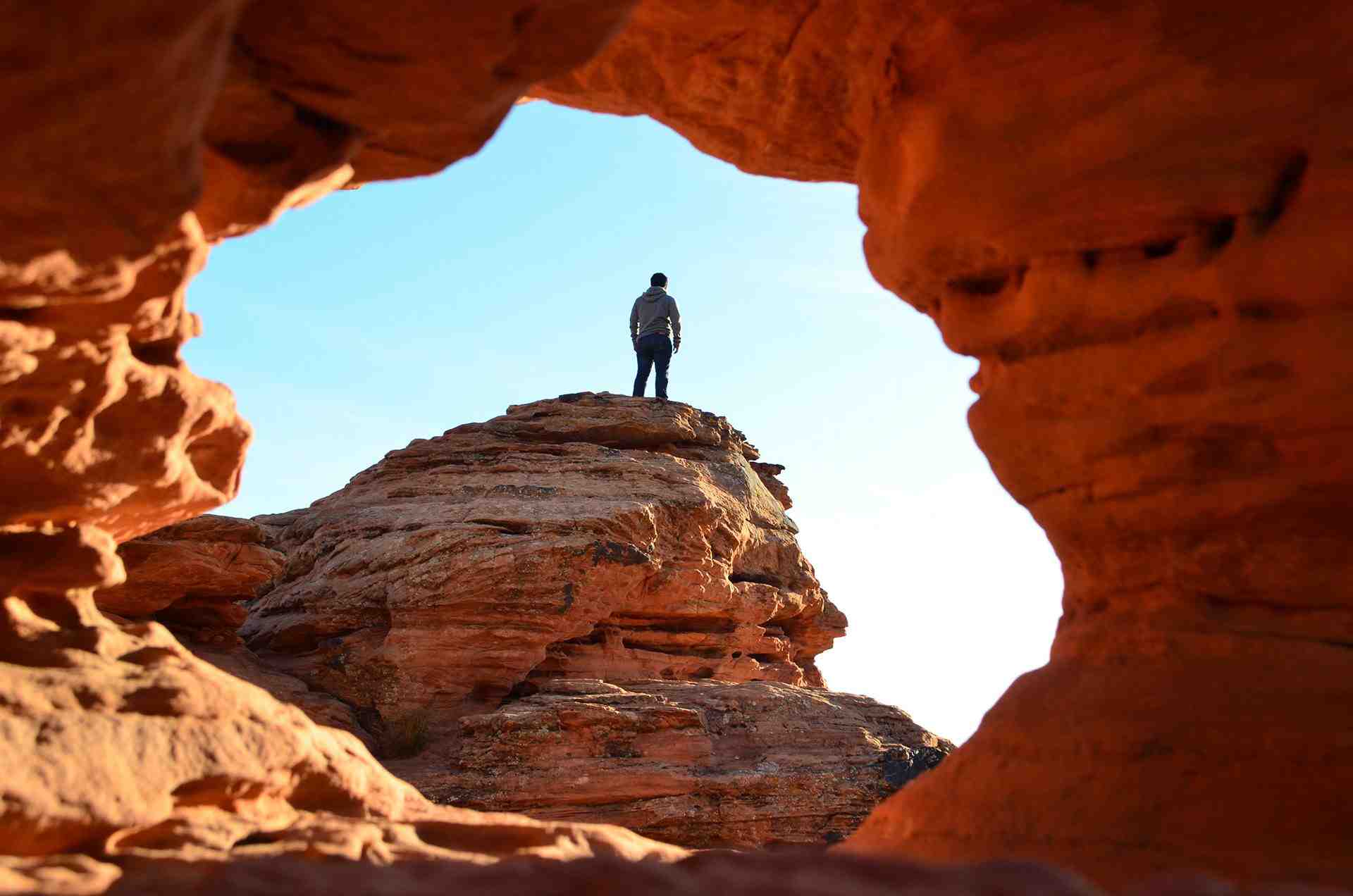 Man Standing triumphantly on top of a boulder through an arch in Snow Canyon National Park in St George Utah