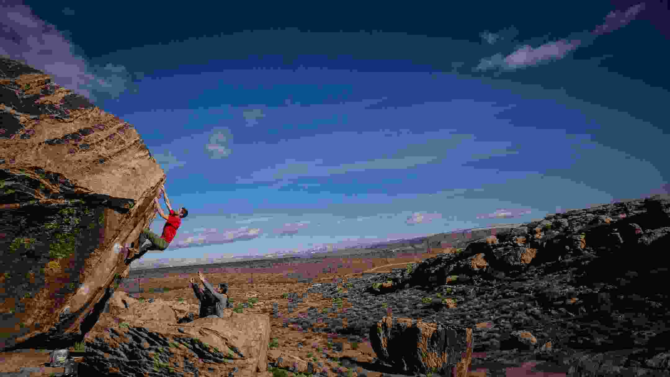 two men boldering up a large boulder with a wide view behind them